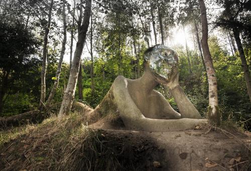 A view of a giant figure sculpture emerging from the ground with a mirrored mosaic face